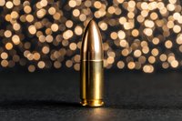 Single 9mm bullet standing upright on dark surface with golden bokeh lights background, symbolizing danger, defense, and firearms concepts.