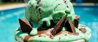 Mint green ice cream scoop with chocolate shavings and wafer cookies on whipped cream base, poolside setting for dessert and summer treat advertising.