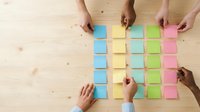 Diverse team hands arranging colorful sticky notes on wooden table for brainstorming session, project planning and creative collaboration in office workspace.