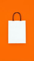 Blank white shopping bag with black handles isolated on vibrant orange background, ready for branding, retail packaging design, e-commerce mockups, and promotional use.