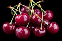 Fresh ripe red cherries with stems and water drops on black background, macro shot showing glossy surface and natural texture of sweet summer fruit.