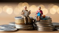 Senior couple figurines sitting on stacks of coins representing retirement planning and financial security for elderly people in golden bokeh background.