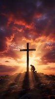 Person kneeling in prayer beside wooden cross silhouetted against dramatic sunset sky with golden light rays breaking through colorful clouds on rocky hilltop.