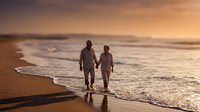 Romantic couple walking hand in hand on beach at sunset with golden light reflecting on wet sand and gentle waves washing ashore during golden hour.