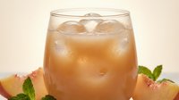 Refreshing peach iced drink in a glass with ice cubes, fresh peach slices and mint leaves on light background.
