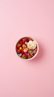 Healthy breakfast bowl with fresh strawberries, granola and ice cream on pink background for food photography and social media content.