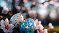 Decorative Easter eggs with gold floral pattern against blooming spring cherry blossoms background, soft bokeh effect creates dreamy seasonal atmosphere.