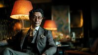 Distinguished Asian businessman in elegant suit sitting confidently in luxurious lounge with warm ambient lighting for corporate and lifestyle concepts.