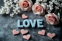 Blue wooden letters spelling LOVE with pink heart decorations and delicate coral roses on dark textured background, romantic Valentine's day or wedding composition.