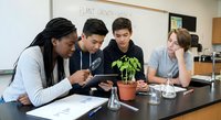 Diverse high school students conducting plant growth science experiment in biology classroom laboratory with seedlings and digital tablet.