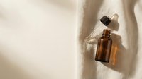 Amber glass dropper bottle with essential oil or serum on natural linen fabric with sunlight shadow, isolated for cosmetics, skincare, wellness product packaging design.