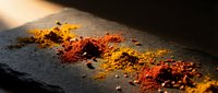 Colorful spice powders scattered on dark slate surface with warm lighting creating dramatic shadows and textures for culinary cooking concepts.