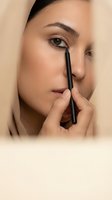 Young Middle Eastern woman applying black eyeliner pencil, close-up beauty portrait with natural glowing skin and neutral tones.