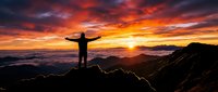 Person with arms outstretched standing on mountain peak at sunrise, silhouetted against dramatic orange and golden sky with clouds below, symbolizing freedom, achievement, and success.