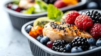 Grilled chicken breast with fresh berries, blueberries, raspberries and blackberries in black plastic container on marble background, healthy meal prep concept.