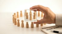 Business professional selecting candidate through magnifying glass with wooden figures representing talent acquisition and human resources recruitment process.