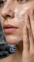 Young woman applying exfoliating face scrub with black particles for skincare routine and beauty treatment at home.