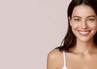 Young woman with bright smile and natural makeup against soft pink background, showcasing healthy skin and positive emotions for wellness or beauty advertising.