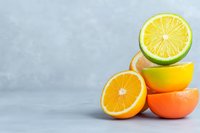 Fresh citrus fruits stacked in creative composition showing orange, lemon and lime halves against light gray background, minimalist food photography.