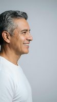 Handsome mature Hispanic man with gray hair smiling in profile wearing white shirt against neutral background for lifestyle and wellness concepts.