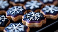 Festive snowflake cookies with dark purple icing and white decorative patterns arranged on baking tray, perfect for winter holiday celebrations.