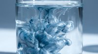 Blue ink or dye dispersing in clear water creating abstract fluid patterns in glass container for creative design projects and artistic concepts.