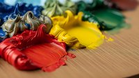 Colorful acrylic paint strokes in red, yellow, blue and green on wooden surface for artistic projects and creative expression.