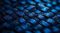 Macro shot of blue woven carbon fiber material showing detailed texture pattern and reflective surface with selective focus and shallow depth of field.