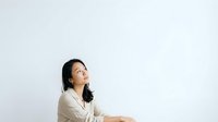 Woman with dark hair wearing beige shirt looking upward thoughtfully against white background, suitable for business, motivation, and contemplation concepts.