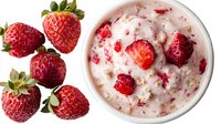 Fresh ripe strawberries and creamy oatmeal porridge with chopped berries in white ceramic bowl, healthy breakfast composition on white background.