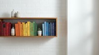 Colorful books arranged by rainbow spectrum on wooden floating shelf against white subway tile wall with decorative vases creating organized home library display.