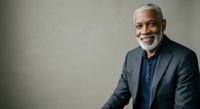 Senior African American male professional with gray beard wearing dark blazer and blue shirt, smiling at camera against neutral background, suitable for corporate portraits, business websites, and professional headshots.