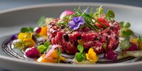 Gourmet beef tartare with microgreens and edible flowers on elegant plate. Fine dining restaurant appetizer with colorful garnish and artistic presentation.