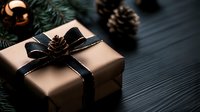 Elegant gift box wrapped in kraft paper with black satin ribbon and natural pine cone decoration against dark wooden background. Holiday season present styling.