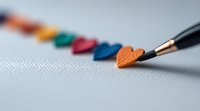 Black pen drawing colorful paper hearts arranged in rainbow sequence on white textured surface, shallow depth of field creates artistic composition for love themes.
