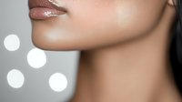 Close up view of feminine chin and glossy lips with smooth skin against blurred bokeh lights background, showcasing natural beauty and skincare concept.