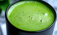 Fresh green smoothie in black cup with frothy texture, rich in nutrients and antioxidants for healthy lifestyle and detox cleansing.
