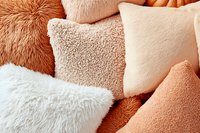 Cozy decorative pillows in trendy coral and neutral tones featuring different textures including faux fur, sherpa, and plush materials for modern home decor styling.