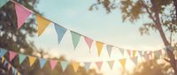 Colorful bunting flags strung between trees at golden hour, creating festive outdoor atmosphere for celebrations, parties, weddings, and garden events.
