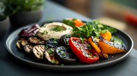 Grilled vegetables and hummus on dark plate with colorful bell peppers, eggplant, zucchini and fresh herbs served as healthy appetizer or main course.