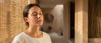 Young woman with dark hair and olive complexion wearing casual white t-shirt in modern bathroom with tile walls, expressing contemplative mood suitable for wellness, lifestyle and mental health content.
