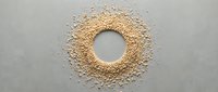 Scattered sesame seeds arranged in circular pattern with empty center on neutral gray background, isolated for design and culinary projects.