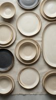 Overhead view of assorted ceramic dinnerware in neutral tones arranged on linen fabric. Includes cream, beige, and charcoal bowls and plates with organic glazed finishes. Perfect for tableware, home decor, and kitchenware design projects.