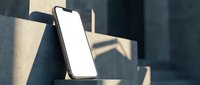 Modern smartphone with blank white screen leaning against concrete wall in natural sunlight. Mobile device mockup for app presentation and digital design.