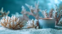 Aromatic candle in glass holder on sandy beach setting with white coral decorations against turquoise background creates serene spa atmosphere.