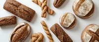 Assorted artisan breads and baked goods arranged on white background, including whole grain loaves, crusty rolls, and twisted breadsticks for bakery, food, and culinary design projects.