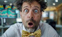 Surprised man with curly gray hair and bright blue eyes wearing yellow polka dot bow tie makes exaggerated shocked facial expression in office setting.