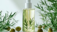 Clear glass bottle with natural olive oil and fresh rosemary sprigs, surrounded by green olives on white background. Organic cosmetic and culinary concept.