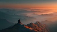 Solitary hiker silhouette sitting on mountain peak at sunrise with layered misty valleys and warm golden light illuminating dramatic landscape for adventure travel.