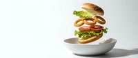 Deconstructed burger with floating ingredients above white plate on clean background. Sesame bun, lettuce, tomato, onion rings and patty separated.